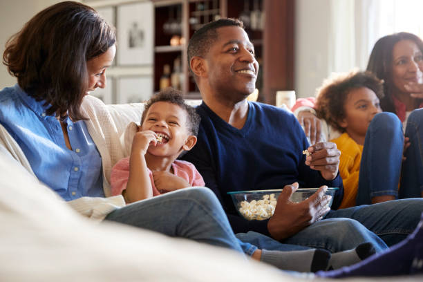 geração três família família sentada no sofá na sala, assistindo tv e comendo pipoca, foco seletivo - men home interior house entertainment - fotografias e filmes do acervo