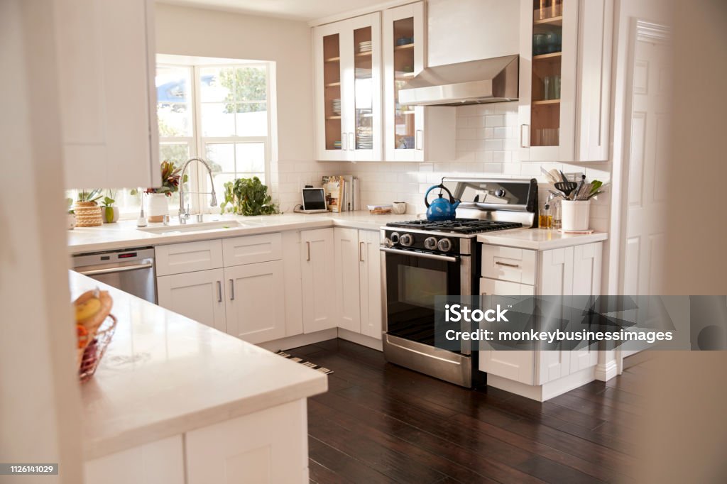 Domestic family kitchen with white furniture and dark wooden floorboards, seen from doorway Kitchen Stock Photo