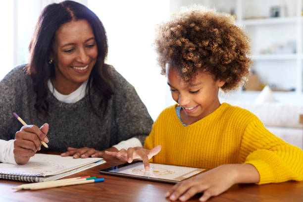 istock Mixed race young grandmother sitting at table doing homework with her granddaughter using a tablet computer, close up 1126143008