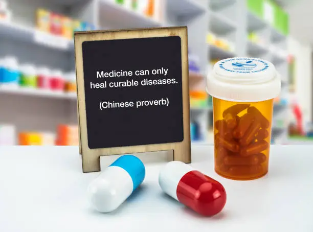 Photo of Informational Sign in a pharmacy, Medicine can only heal curable diseases. (Chinese proverb),  on a whiteboard next to bottles of medicines, conceptual image