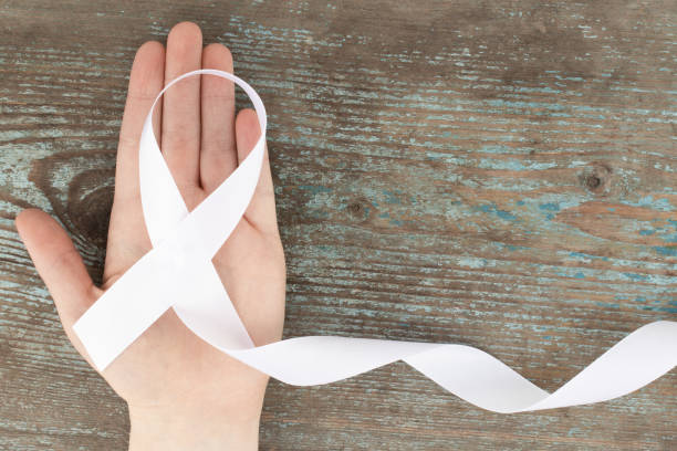 white ribbon on the wooden background with copy space. White or light pearl color ribbon for raising awareness on Lung cancer, Bone cancer, Multiple Sclerosis, Severe Combined Immune Deficiency Disease (SCID) and Newborn Screening  symbol stock photo