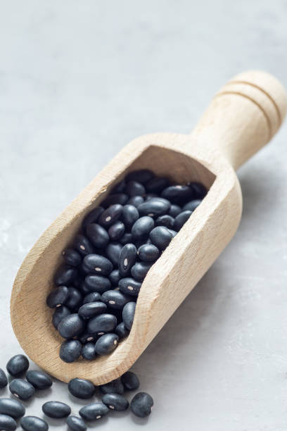 istock Black beans in a wooden scoop on gray concrete background, vertical, copy space 1126149930