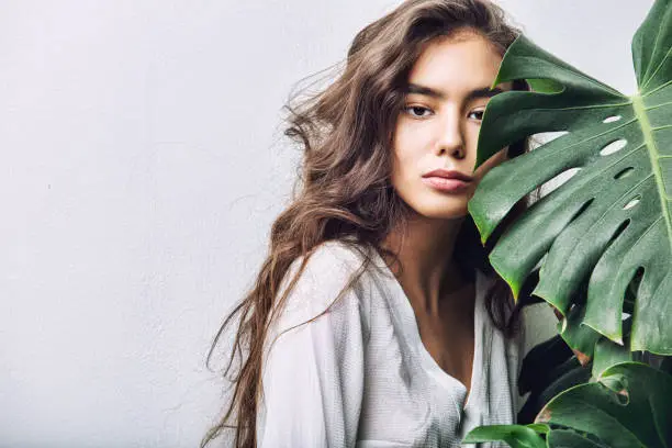 Young beautiful girl model Asian brunette with long hair posing in Studio with tropical plant on isolated background