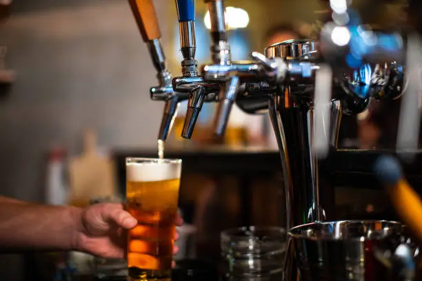 Bartender Pouring Glass of Beer For Customer at Bar, unrecognizable person