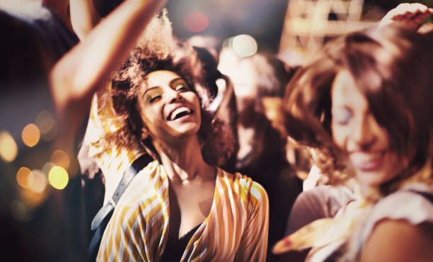 Ecstatic night out. Two young women dancing and jumping at the music festival. They raised their arms and cheer to the music. only young women stock pictures, royalty-free photos & images