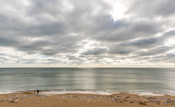 Barton on Sea, England - October 27, 2018: Sea with clouds and glistening water and running child and man at the beach.