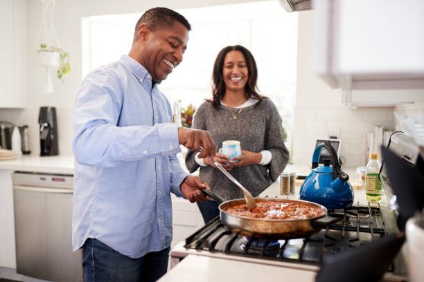 istock Millennial Hispanic man standing in the kitchen cooking with his partner standing beside him, backlit 1126173514