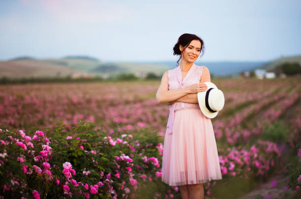 schöne junge frau mit strohhut blick auf sonnenuntergang im feld rosen. aroma, kosmetik und parfüm-werbung. - human hair women horizontal rose petals stock-fotos und bilder