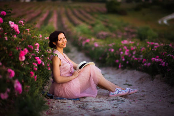 schöne junge frau mit dunklen haaren sitzen im feld rosen. aroma, kosmetik und parfüm-werbung. - human hair women horizontal rose petals stock-fotos und bilder