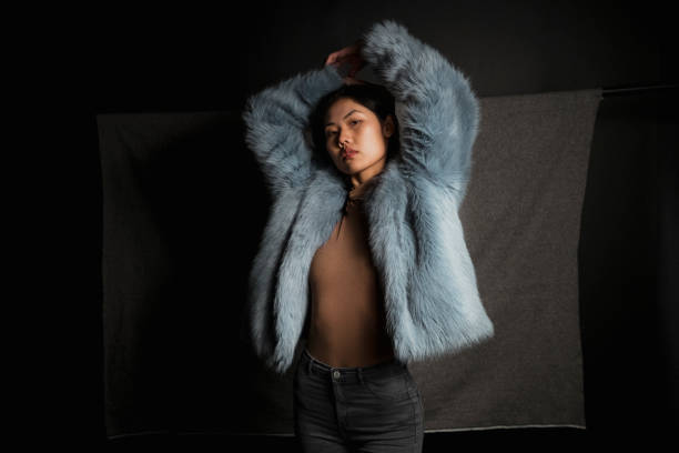 Alternative Posing Portrait of a young female fashion model. She is standing in front of a grey studio background. mink fur stock pictures, royalty-free photos & images