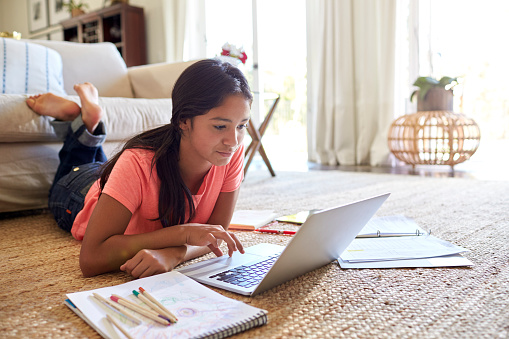 Adolescente, tendido en el suelo en la sala de estar haciendo su tarea con un ordenador portátil, ángulo bajo, de cerca photo