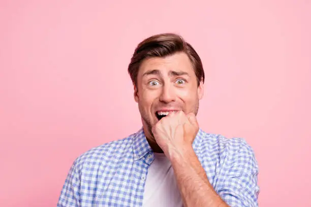 Photo of Close-up portrait of attractive handsome puzzled guy wearing checked shirt biting nails waiting lottery winning isolated over pink pastel background