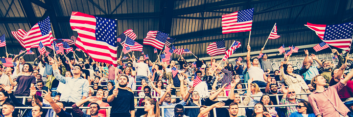 Large group of American fans waving their flags on a stadium during a sporting event.