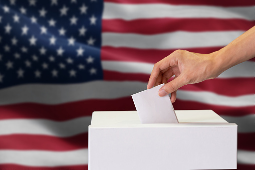 Primer plano de hombre casting e insertar un voto, elegir y decidir lo que quiere en la caja de votación con la bandera de Estados Unidos en el fondo. photo