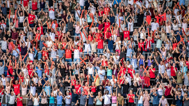 Sports fans in red jerseys cheering on stadium bleachers Large crowd of people, some wearing red sports jerseys, cheering and clapping on stadium bleachers. bleachers photos stock pictures, royalty-free photos & images