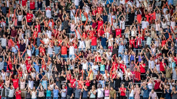 Photo of Sports fans in red jerseys cheering on stadium bleachers