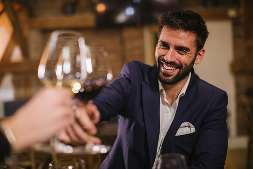 Young businessman drinking wine in winery with friends, smiling lively