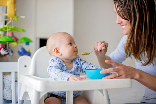 Cute little baby boy, eating mashed vegetables for lunch, mom feeding him, sweet toddler boy, smiling