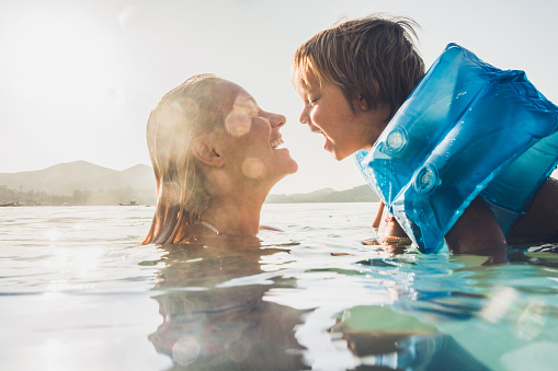 Carefree small boy and his mother enjoying in summer day while having fun in the sea.