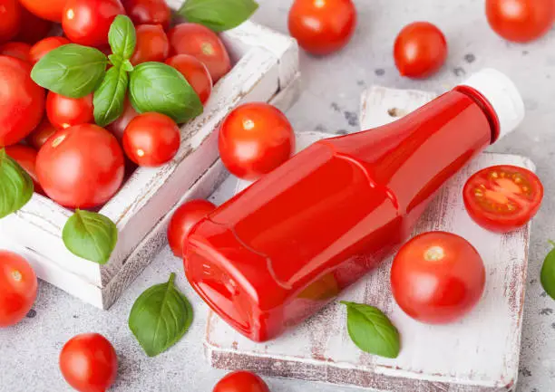 Photo of Plastic container with tomato ketchup sauce with raw tomatoes on kitchen stone background.