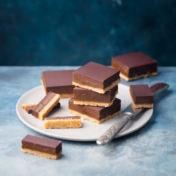 Photo of Chocolate caramel slices, bars, millionaires shortbread on a plate. Blue background. Copy space.