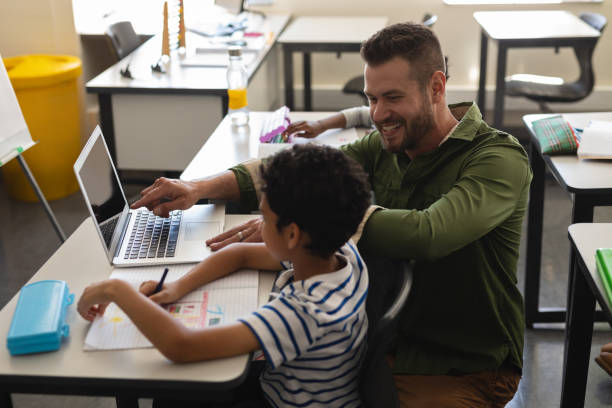 istock Young school teacher helping boy with study on laptop in classroom 1126206885