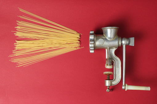 Vintage meat grinder and pasta on red background, top view, minimalism
