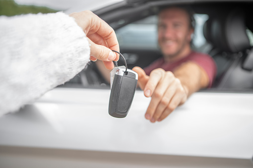 Caucasian young man sitting at the steering wheel inside car accepting car keys from man point of view