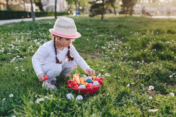 беззаботная маленькая девочка, играющая с корзиной, полной пасхальных яиц - child easter flower little girls стоковые фото и изображения