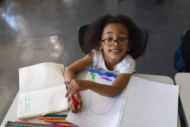 istock High angle view of schoolgirl drawing in book while looking at camera in classroom 1126232313