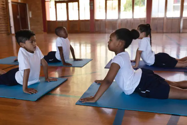 Side view of concentrate schoolkids doing yoga position on a yoga mat in school