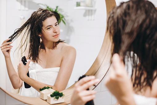 Cuidado del cabello y cuerpo. Mujer joven feliz en toalla blanca aplicando acondicionador máscara de pelo en el baño, espejo de reflexión. Mujer sexy delgada con la piel natural disfrutando de spa y bienestar, relajante photo