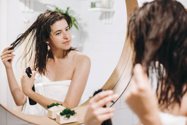 cura dei capelli e del corpo. giovane donna felice in asciugamano bianco che applica maschera balsamo sui capelli in bagno, riflesso dello specchio. donna sexy magra con pelle naturale godendo di spa e benessere, rilassante - cura dei capelli foto e immagini stock