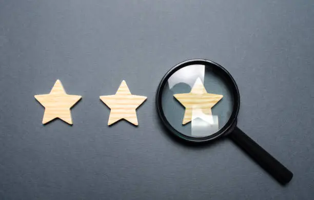 Photo of Three stars and a magnifying glass on a gray background. Authentication of the third star, rating fraud. Rating and status of the restaurant or hotel. Prestige.. High quality and reliability