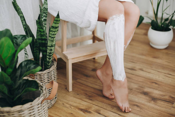 머리 제거 개념, 탈모 크림입니다. 녹색 식물으로 집 욕실에서 그녀의 다리에 면도 크림을 적용 하는 흰 수건에 젊은 여자. 피부 관리 및 웰빙 개념입니다. - human leg smooth human skin human foot 뉴스 사진 이미지