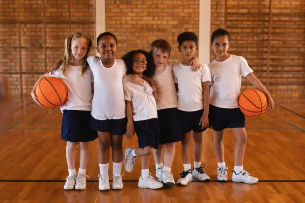 Front view of schoolkids standing and looking at camera at basketball court in school