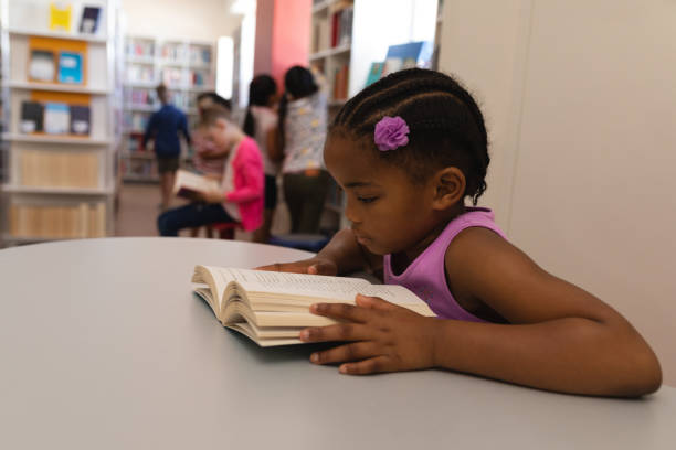 livro de leitura colegial na mesa na biblioteca da escola - africa child reading african descent - fotografias e filmes do acervo