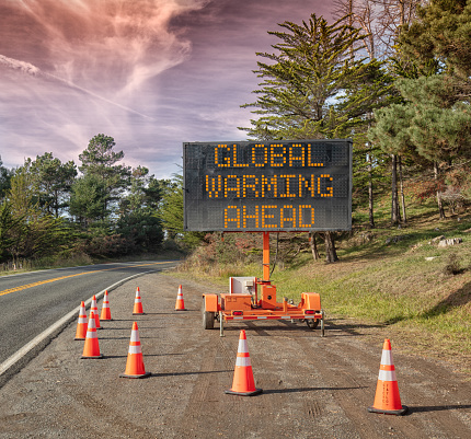 Global  Warming AHEAD:  This is a photograph of a mobile roadside sign parked on highway one in northern California. It is a trailer and powered by batteries and provides information and warnings for drivers by displaying words on a large panel display.