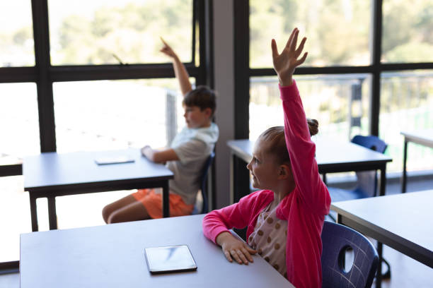 istock School kids raising their hand while sitting at desk in classroom 1126250064