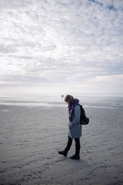 istock Young woman in coat walking on winter beach 1126255519