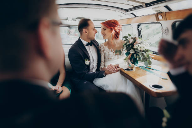 stylish happy bride and groom embracing,gently hugging in retro car and smiling. emotional moment, space for text. luxury wedding newlyweds couple, honeymoon travel