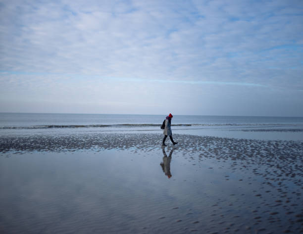 Young woman in coat walking on winter beach of St.Peter Ording, North Sea, Germany