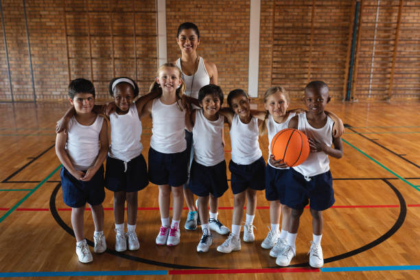 Happy schoolkids and female coach looking at camera at basketball court Front view of happy schoolkids and female coach looking at camera at basketball court in school 9 stock pictures, royalty-free photos & images