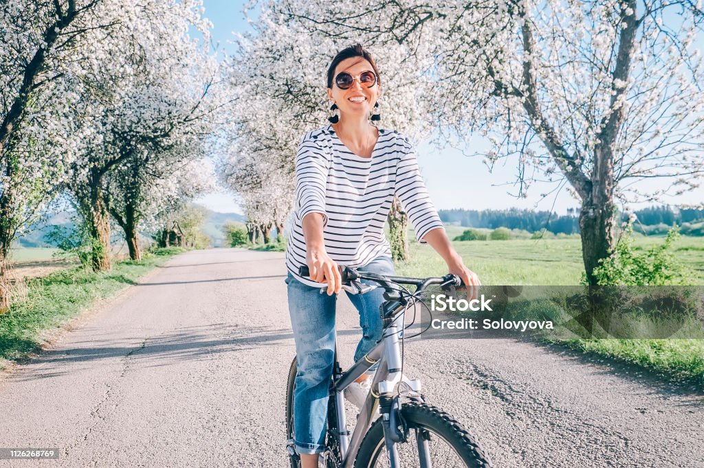 Happy smiling woman rides a bicycle on the country road under blossom trees. Spring is comming concept image. Springtime Stock Photo