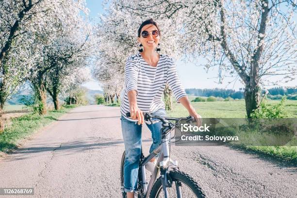 Happy Smiling Woman Rides A Bicycle On The Country Road Under Blossom Trees Spring Is Comming Concept Image Stock Photo - Download Image Now