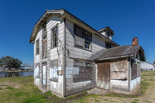 Side angle of abandoned and derelict building on green grass with clear blue sky