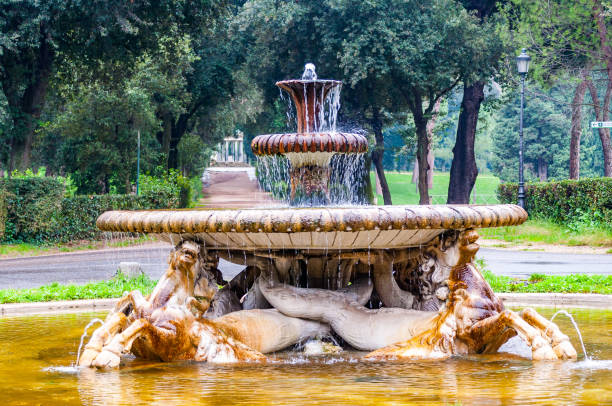 18th century fontana dei cavalli marini stands in the middle of a round plaza surrounded by trees and walkways at via pinciana main entrance of the borghese gardens - stone textured italian culture textured effect imagens e fotografias de stock