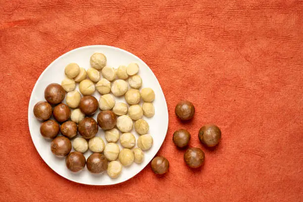 macadamia nuts on a white plate against red textured paper background with a copy space