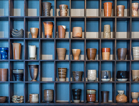 Various and colorful ceramic mugs on modern wooden shelf on blue background.