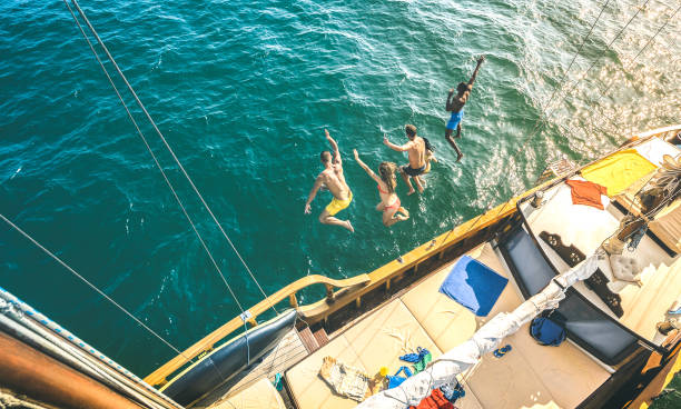 vista aerea di felici amici millenari che saltano dalla barca a vela durante il viaggio sull'oceano marino - ragazzi e ragazze ricchi che si divertono insieme nell'esclusiva giornata di festa in barca - concetto di vacanza di lusso sul filtro luminoso a co - cruise cruise ship nautical vessel florida foto e immagini stock